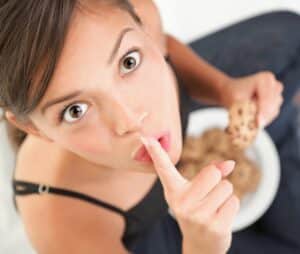 woman eating sweets and holding her finger to her lips suggesting it's a secret